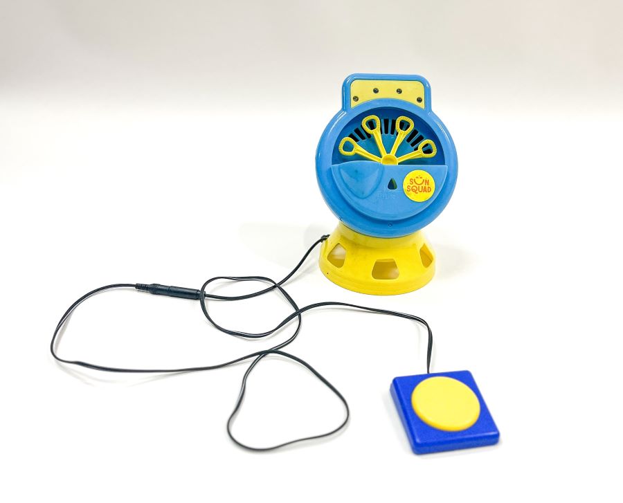Blue and yellow bubble machine with a black connecting wire attached to a large blue switch with a large round yellow button.