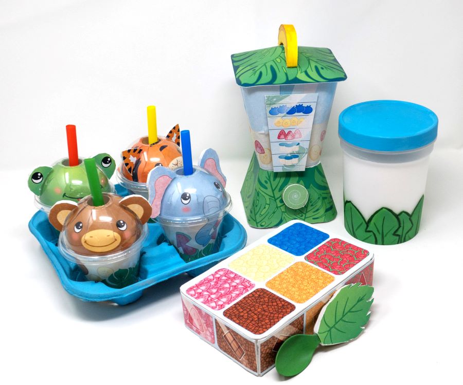 Colorful children’s imaginative-play smoothie-shop prototype made of paper. Play set includes: four animal-faced cups with straws, in a blue carry-tray; a blender; a white container with a blue lid; and a box resembling an ingredients’ container.