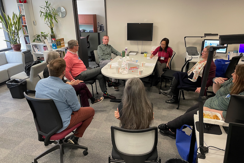 A group of faculty members gathered around a table in a bright office space for a meeting.