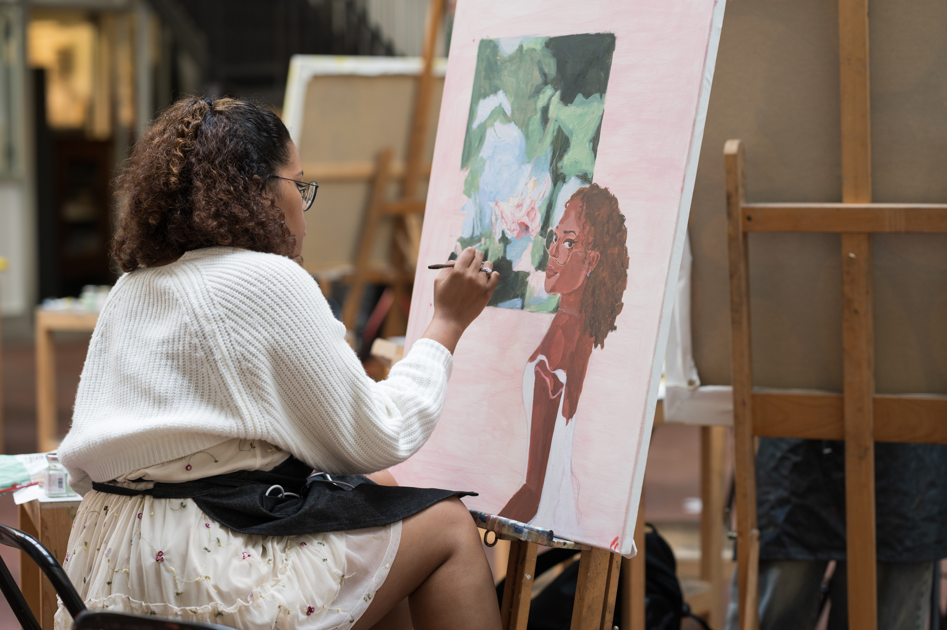 A student paints a portrait in a studio, focused on her colorful canvas.