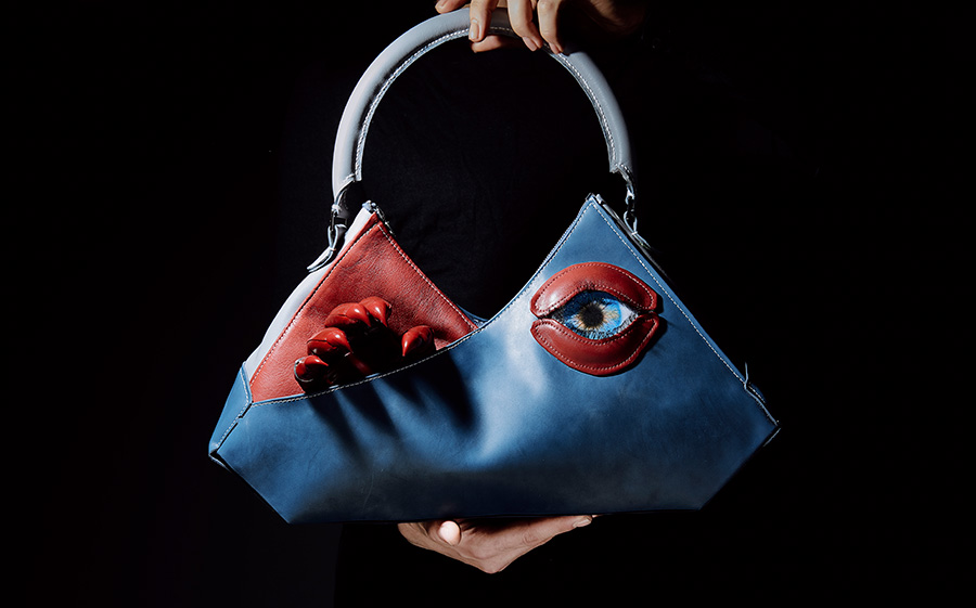 blue handbag with protuding, red fingers and an eye encased in red lips as details
